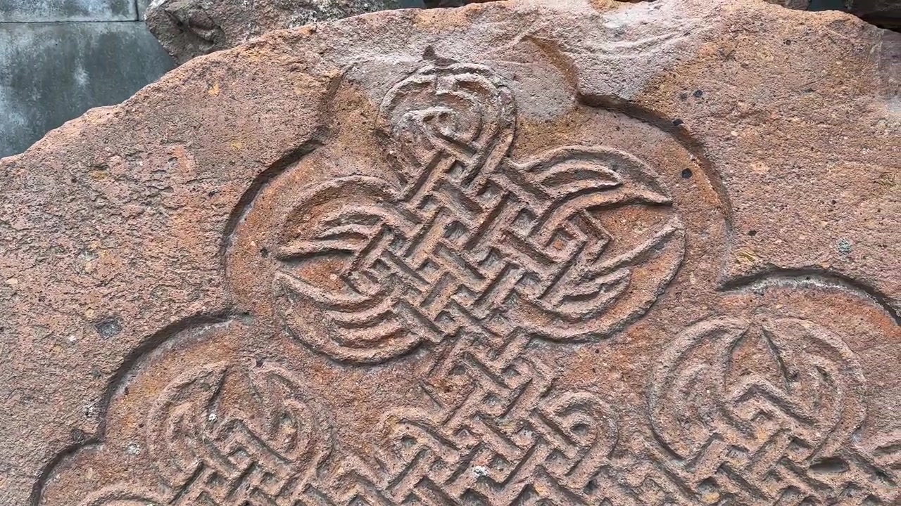 Oranžovo-růžový kámen ve starobylém náhrobním hrobě arménských hřbitovních ruin, kostel, kaple, klášter, křížová řezba, zdivo z tufu, historické středověké posvátné náboženské dědictví, turismus, zvětralá krajina.