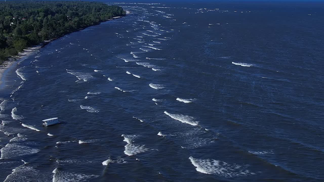 Waves roll on the surface of the Baltic Sea near coastal landscape