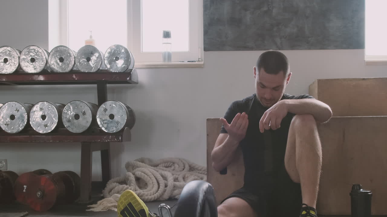 un joven descansa en el suelo y bebe agua después de hacer ejercicio en el gimnasio