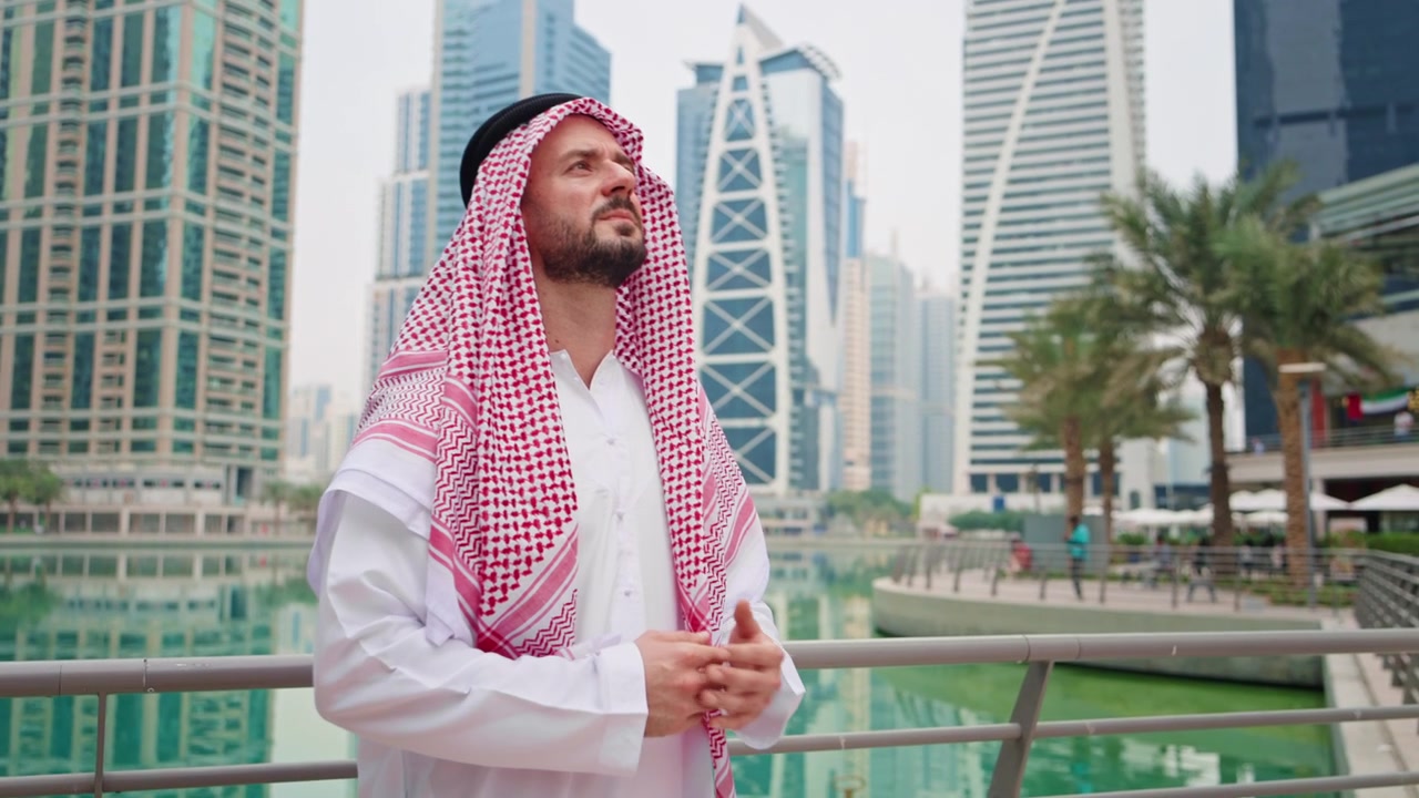 Uomo d'affari arabo in abito tradizionale e copricapo che osserva edifici moderni mentre è in piedi