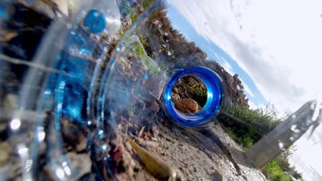 discarded plastic bottles litter the ground and roll in the wind - trash polluting the environment as seen from inside a water bottle