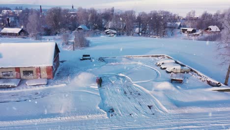 Person-cleaning-snow-from-parking-lot-near-old-rural-farm-building-during-snowfall