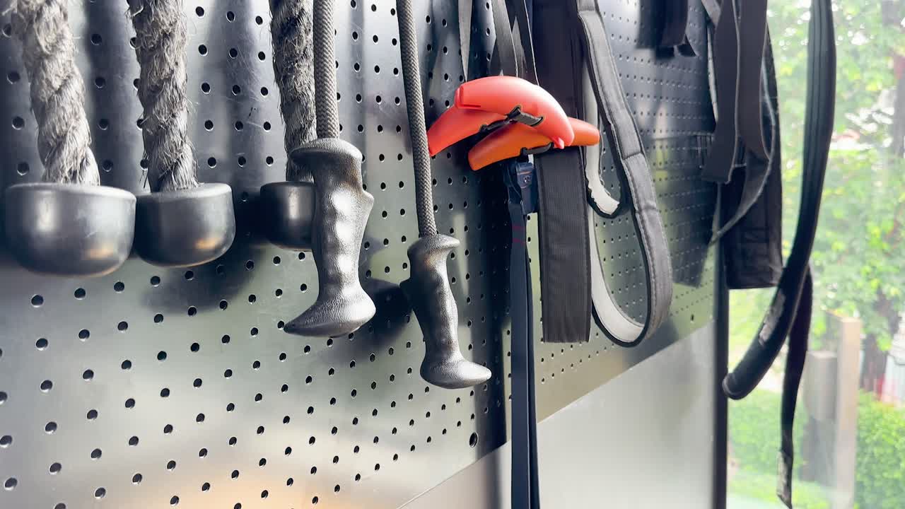 Camera pans across gym rope handles, attachments, and accessories on pegboard in bright natural light
