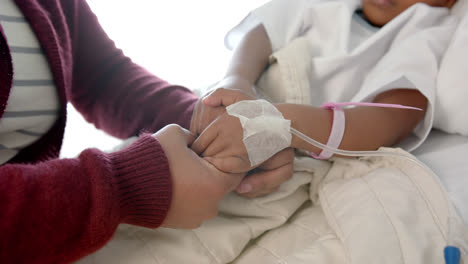 holding hands of african american mother and daughter lying in hospital bed, slow motion