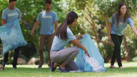 grupo feliz diverso de amigos masculinos y femeninos poniendo basura en bolsas de basura azules en el parque