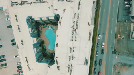 drone footage of an apartment complex with a pool, alongside a busy road with traffic