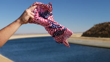 a red white and blue american flag bandana flying in the strong wind in slow motion with the california aqueduct in the background