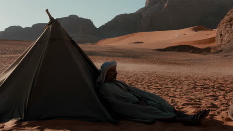 man rests by a tent in the vast desert