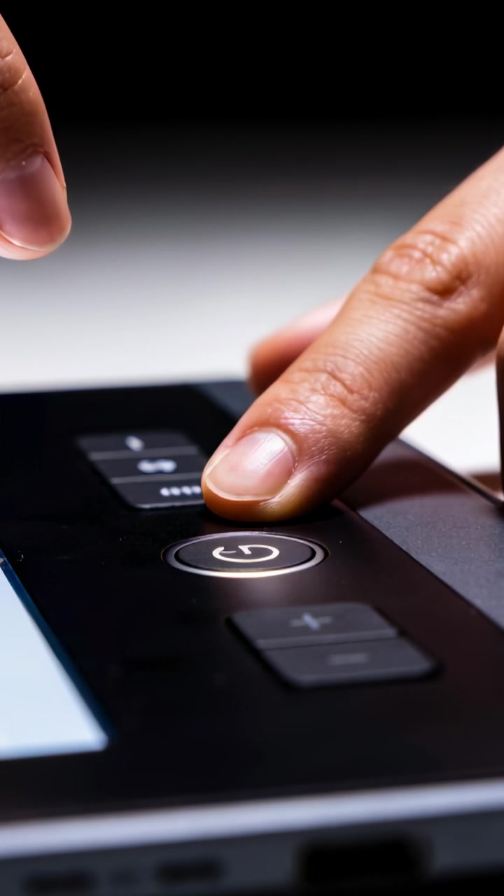 Video verticale: Punta dell'indice destro che preme il pulsante di accensione su una console, attivando il dispositivo.