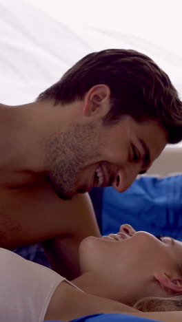 una pareja joven acostada en la cama hablando.