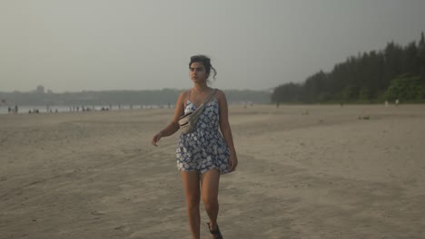 mujer en un vestido de verano caminando por una playa de arena durante un día nublado