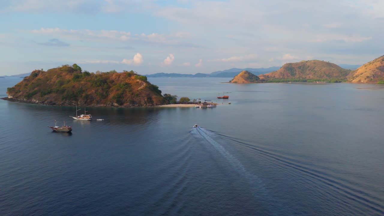 Wide aerial shot of a speedboat returning to shore with small islands and anchored boats in the background