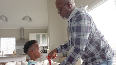happy african american grandfather and grandson holding hands and smiling at home, slow motion