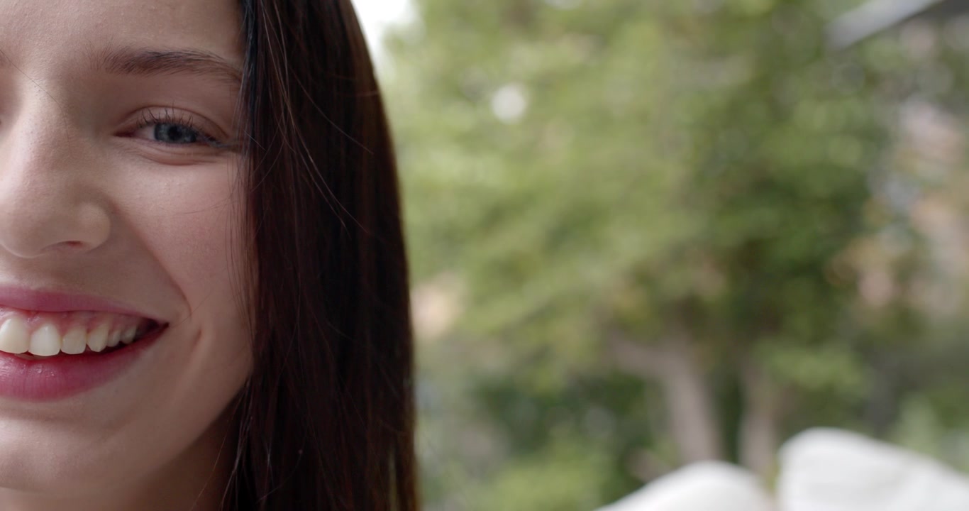 Adult female holding neutral, shifting into laughing after offscreen cue, patio foliage, copy space
