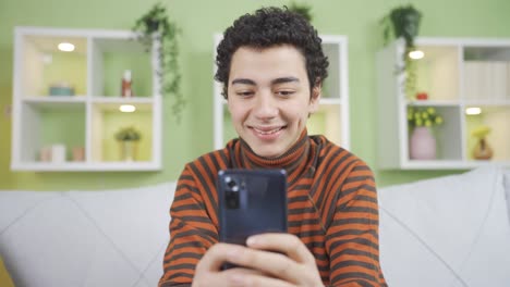 Adolescent-boy-using-phone-at-home,-cheerful-and-smiling.