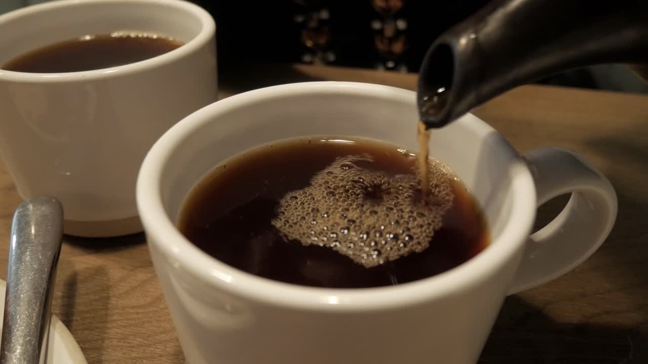A steaming cup of English Breakfast tea being poured into a white mug indoors