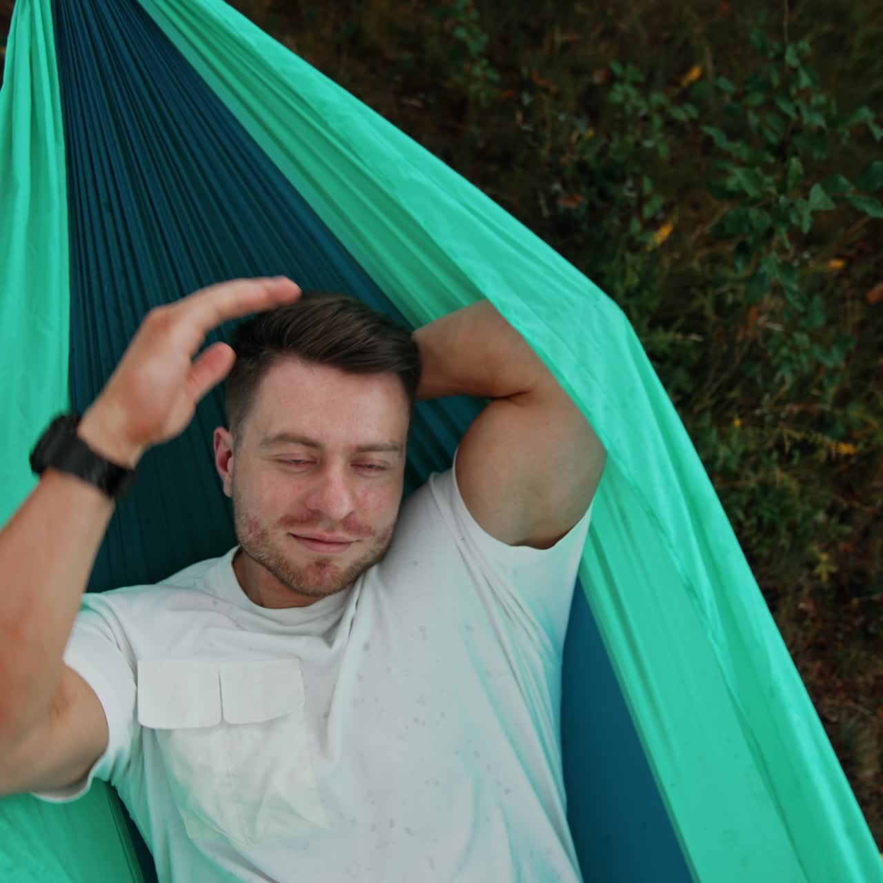 Un uomo caucasico sorridente e rilassato è comodamente sdraiato su un'amaca. L'uomo si sta godendo una vacanza nella natura. Vista dall'alto