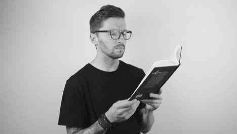 footage of a tattooed man with a full sleeve and wristband wearing glasses and searching something from a book