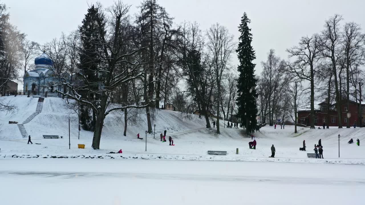 Winterdag met mensen die sleeën van een besneeuwde heuvel in een stadspark met sneeuwval, luchtfoto schuift naar rechts