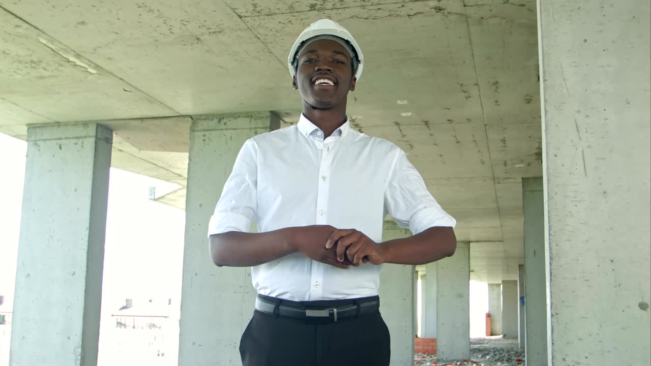 hombre de negocios africano riendo en la zona de construcción presentando algo mirando a la cámara