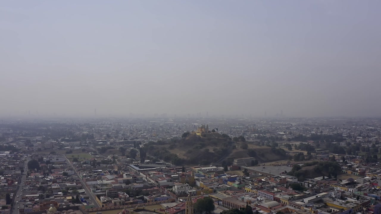An aerial drone shot captures the iconic Santuario de Nuestra Señora de los Remedios (Church of Our Lady of Remedies) perched atop the Great Pyramid of Cholula in Puebla, Mexico.