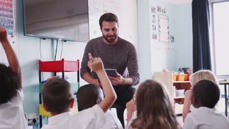 maestro masculino con una tableta digital enseña a un grupo de alumnos de primaria uniformados en el aula de la escuela
