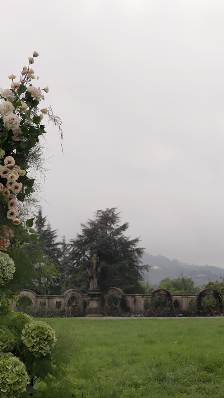 Serene Garden View with Historic Stone Wall, Statue, and Floral Arch