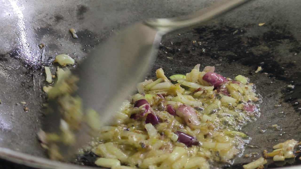A chef is sautéing sliced onions in a hot wok using palm oil, creating a wonderful, savory aroma. The cooking process is a key step in preparing an appetizing meal