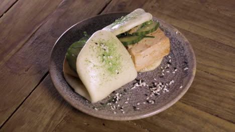 Pan-of-a-plate-of-steamed-tofu-bao-buns-on-a-handmade-plate-and-wooden-table