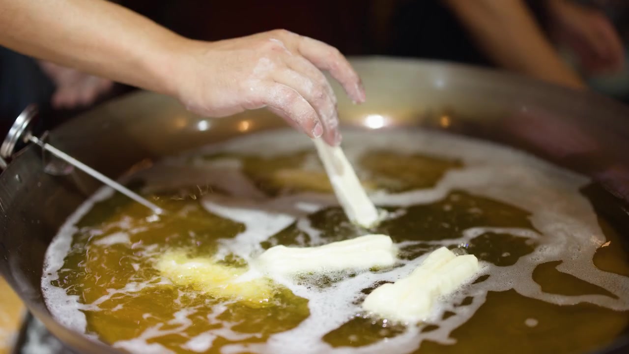 Close-up of hands placing dough into bubbling oil to cook traditional Asian street food.