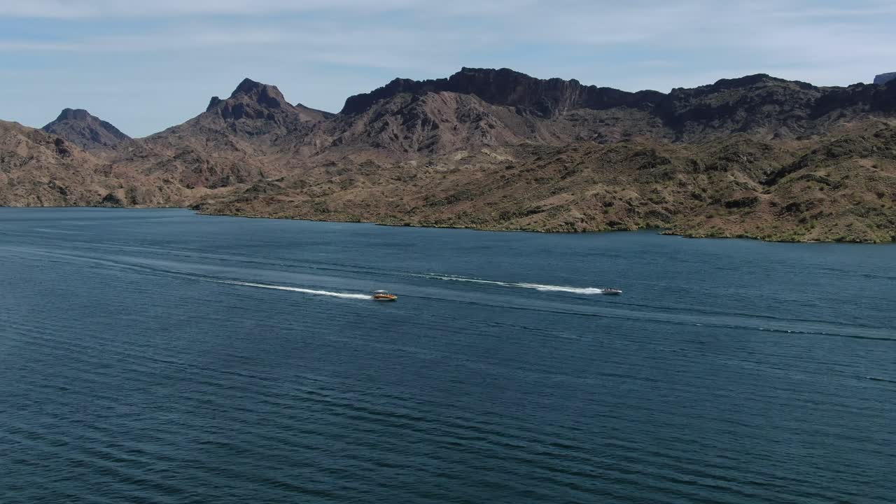 고해상도 4k 드론 영상은 여름에 애리조나-캘리포니아 사막에서 화창한 날 친구 및 가족과 즐거운 시간을 보내는 두 척의 고속 보트가 하바수 호수를 가로질러 전속력으로 경주하는 것을 보여줍니다.