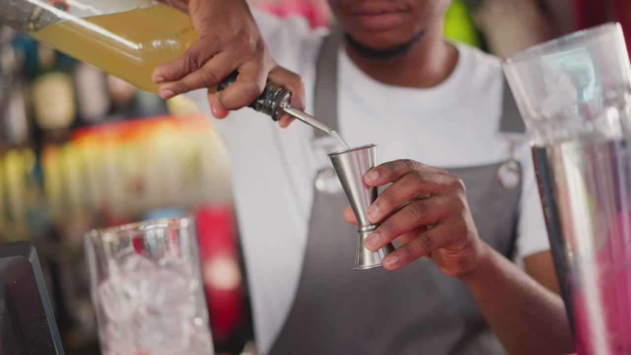 흑인 바텐더가 술집에서 테일을 위해 알코올 성분을 준비합니다. 젊은 남자가 카운터에서 음료를 만들고 있습니다.