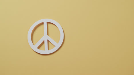 Close-up-of-white-peace-sign-and-copy-space-on-yellow-background