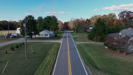 black and white cars on rural road in suburb of usa. houses and homes with green grass fields in autumn. drone forward wide shot.