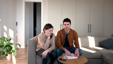 blind man reading a braille book aloud and his girlfriend listening him while sitting on sofa at home