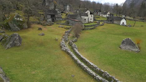 Drone-Aéreo-De-Arriba-Hacia-Abajo-Disparado-Sobre-El-Límite-Rocoso-Al-Lado-De-Casas-De-Pueblo-En-Cavergno,-Distrito-De-Vallemaggia-En-El-Cantón-De-Ticino,-Suiza-Durante-El-Día