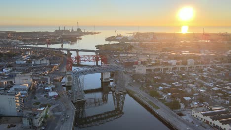 Cinematic-harbour-view-capturing-transporter-bridges-over-Riachuelo-Matanza-river-with-beautiful-sunrise-above-horizon,-La-Boca-neighbourhood-and-connecting-sea-Rio-de-La-Plata