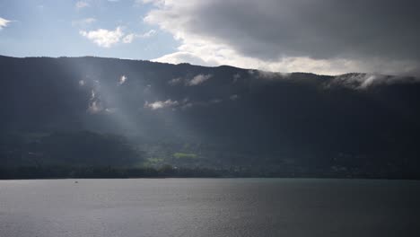 Lake-Annecy-with-god-light-rays-in-front-of-lush-green-mountains-in-the-French-Alps,-Wide-shot