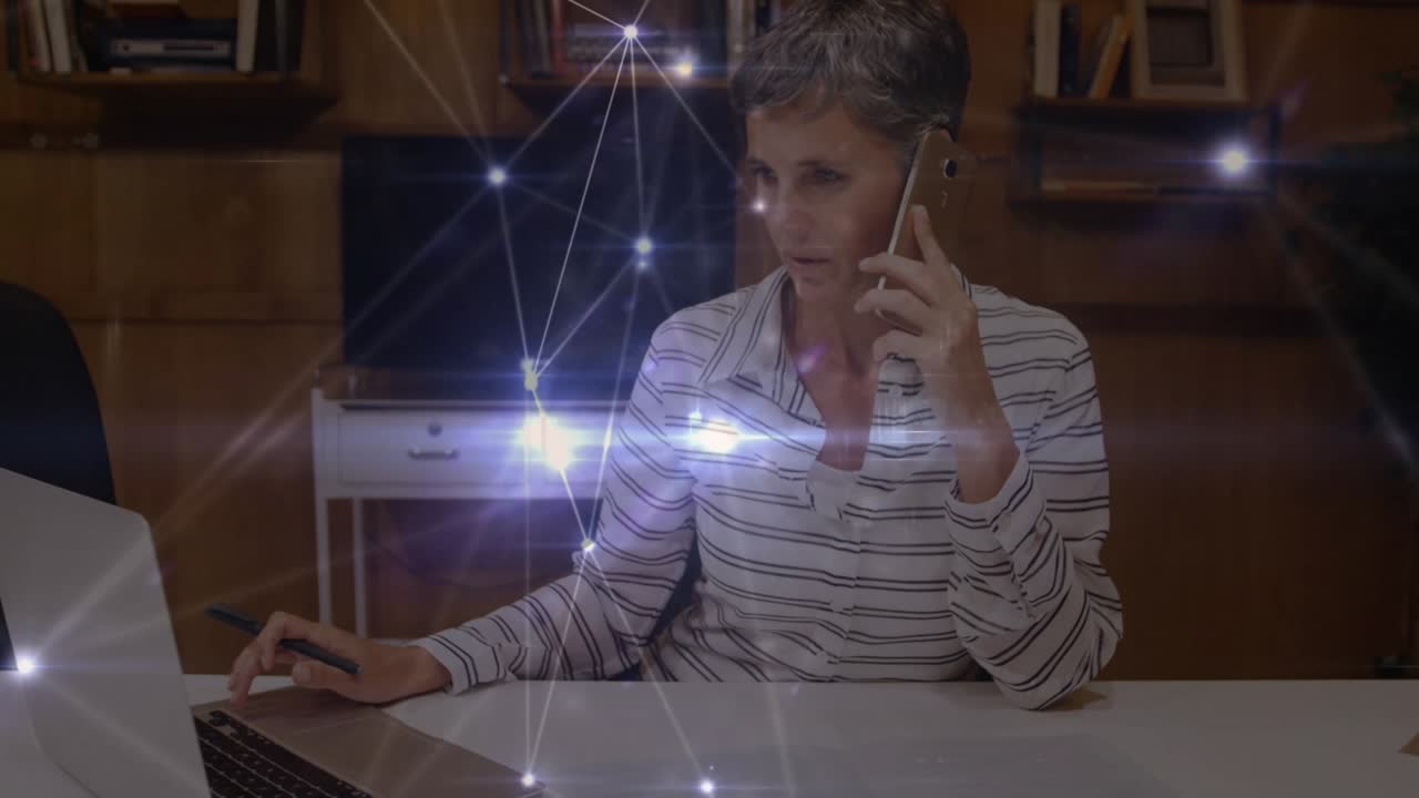 Network of connections over caucasian senior businesswoman using laptop and talking on smartphone