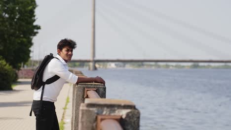 young asian student, businessman with backpack, enjoying riga city view at river