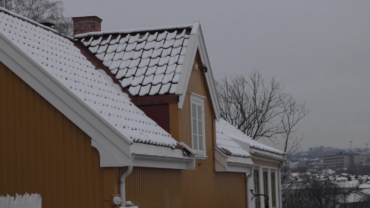 Scenic view of traditional residential houses and buildings in Oslo, Norway, with tiled roofs and yards covered in white snow on a quiet, gloomy winter day in a Scandinavian neighborhood.