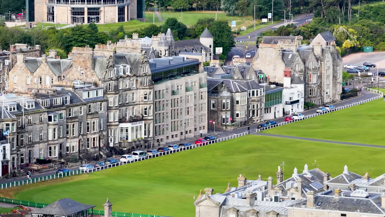 Smooth aerial pan reveals historic architecture, green golf course, and urban landscape in daylight