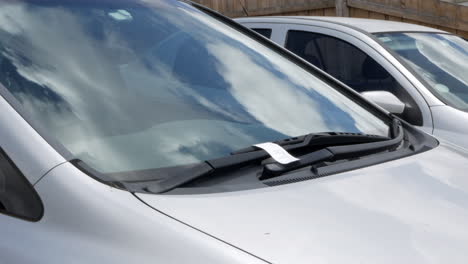 man discovers a parking ticket under the window wipers of his car