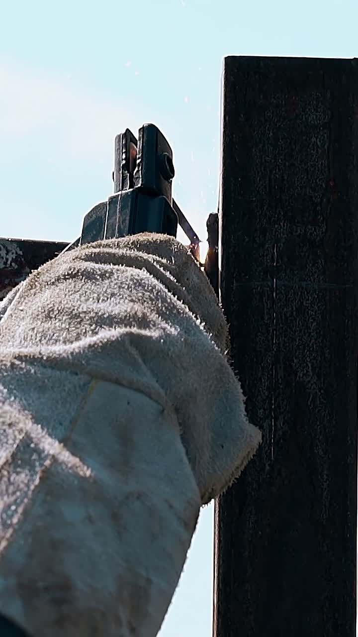 closeup welder in textile special gloves fixes metal carcass parts of country house fence against sky