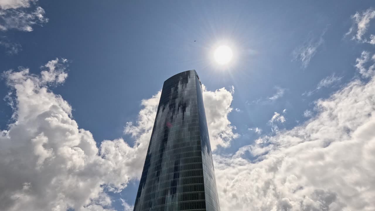 Low angle view of tall glass skyscraper with clouds drifting in sky