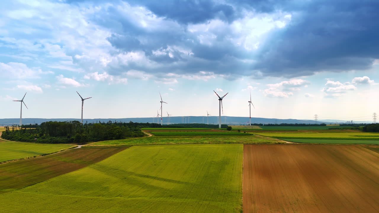 Dramatic cloudscape cover the sky over the fields. Wind turbines produce clean energy