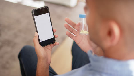 hombre biracial sosteniendo medicamentos haciendo una llamada de video usando teléfono inteligente, espacio de copia, cámara lenta