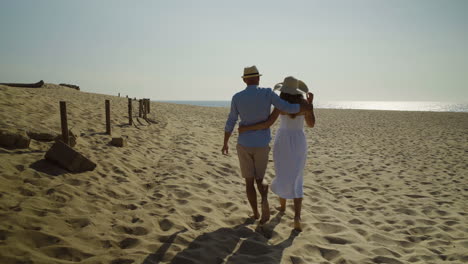 Back-view-of-couple-walking-on-sandy-beach