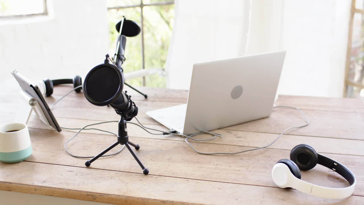 Podcast setup with laptop, microphone, and headphones on wooden desk at home