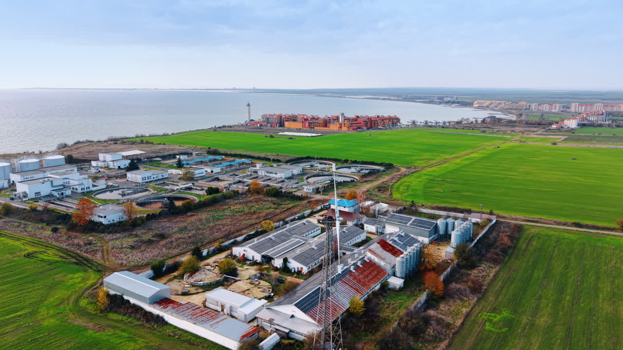 Approaching the industrial area with large warehouses covered with solar panels. Water treatment plant and seascape at backdrop